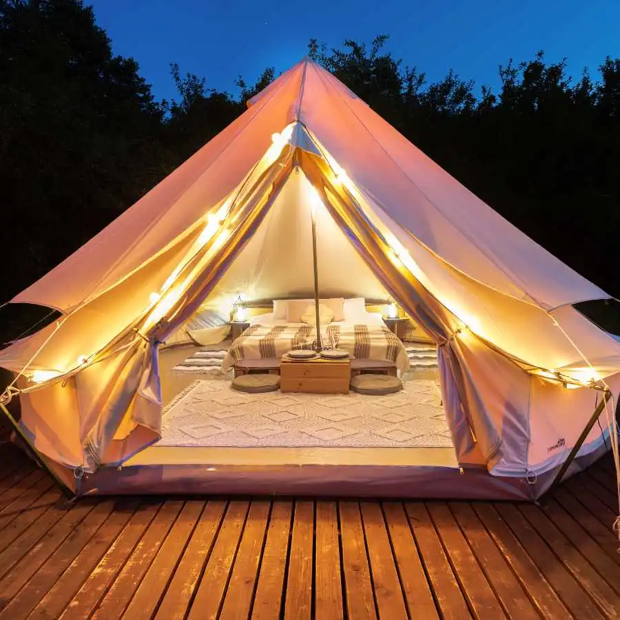 Tenda glamping arredata con letto matrimoniale e luci soffuse su pedana in legno, immersa nella natura al tramonto.