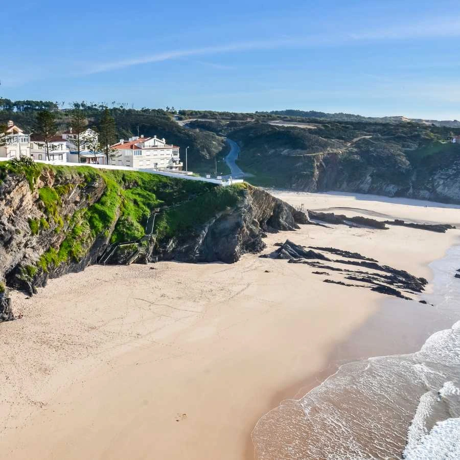 Spiaggia tranquilla sulla costa dell'Alentejo con scogliere verdi e case bianche