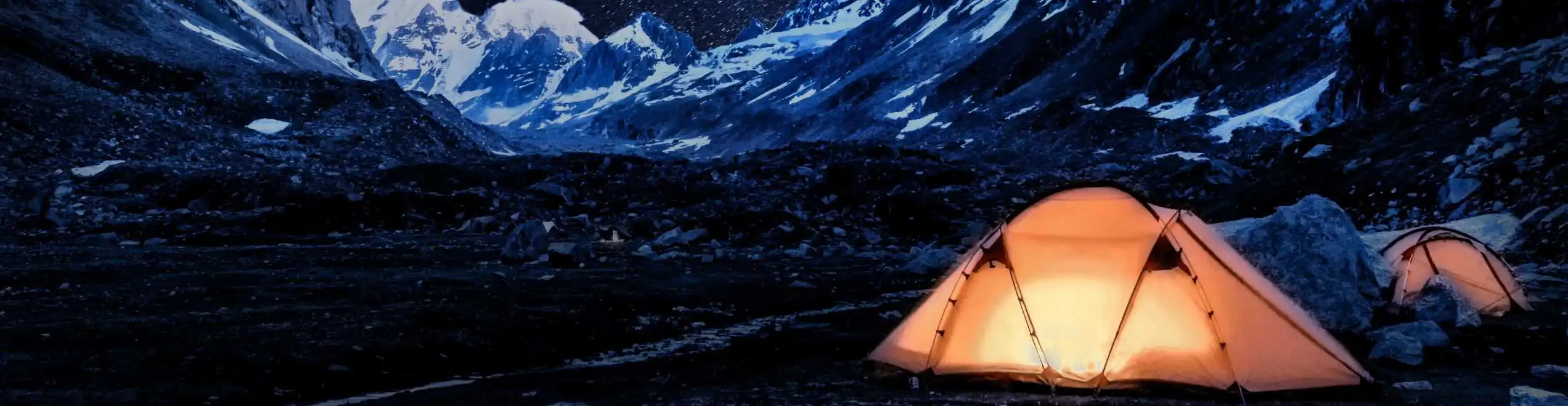 Tende illuminate di notte ai piedi di montagne innevate, perfette per un’esperienza di glamping sotto le stelle.