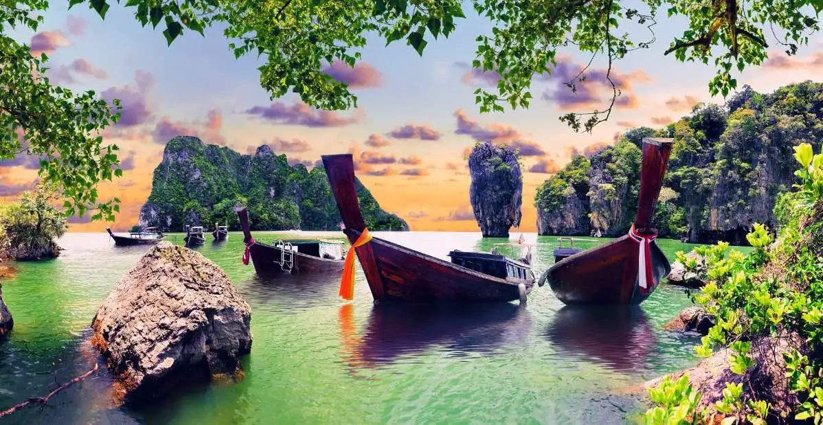 Barche tradizionali thailandesi (longtail boat) ormeggiate in un'insenatura verde smeraldo con formazioni rocciose calcaree e isolotti verdi, Baia di Phang Nga, Thailandia.