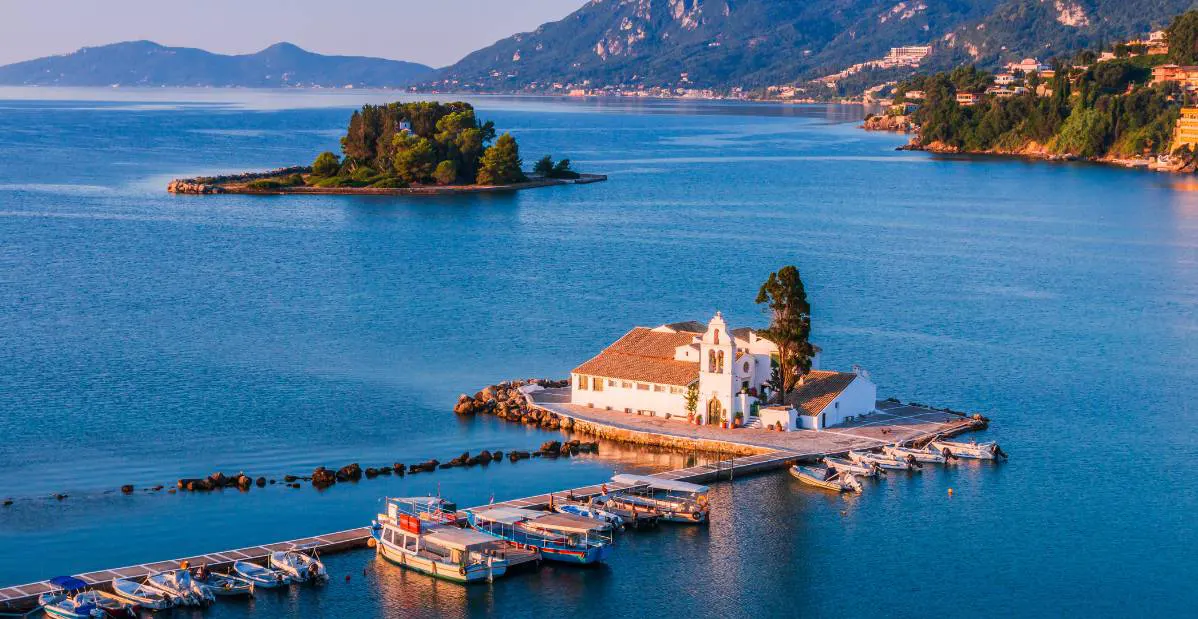 Monastero di Vlacherna a Corfù visto dall’alto, circondato dal mare turchese e piccole barche ormeggiate.