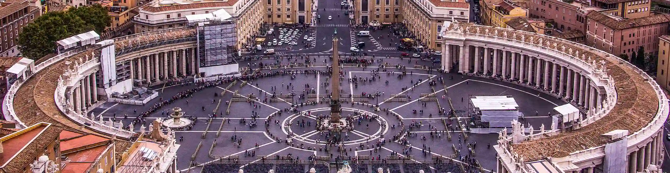 Panorama di Piazza San Pietro in Vaticano vista dall’alto, con folla di visitatori e colonne monumentali.