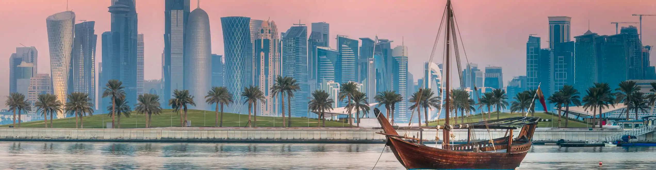Skyline di Doha al tramonto con dhow tradizionale sul mare, tra modernità e cultura del Qatar.