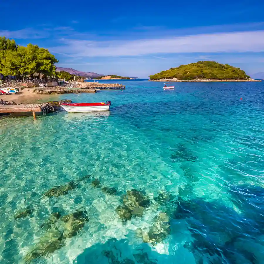 Barca su mare cristallino con fondale visibile e isolotto lungo la costa dell’Albania