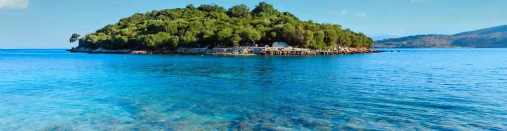 Isolotto verde a Ksamil con mare turchese cristallino e acqua limpida lungo la costa dell’Albania