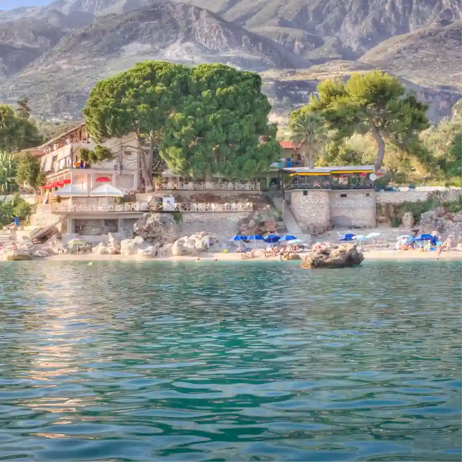 Villaggio sulla costa della Riviera albanese con spiaggia, mare calmo e montagne sullo sfondo