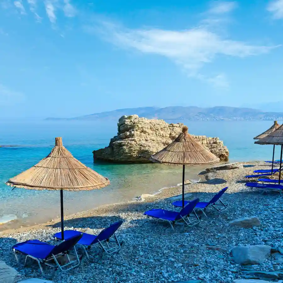 Spiaggia in Albania con ombrelloni, lettini e mare cristallino lungo la costa rocciosa