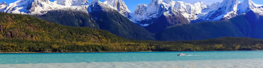 Paesaggio in Alaska con lago turchese, foreste e montagne innevate sullo sfondo