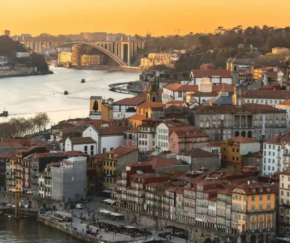 Offerta viaggio Portogallo Classico: pacchetto vacanza tra Porto e città storiche Panorama di Porto al tramonto con il fiume Douro, il ponte e le case storiche sul lungofiume