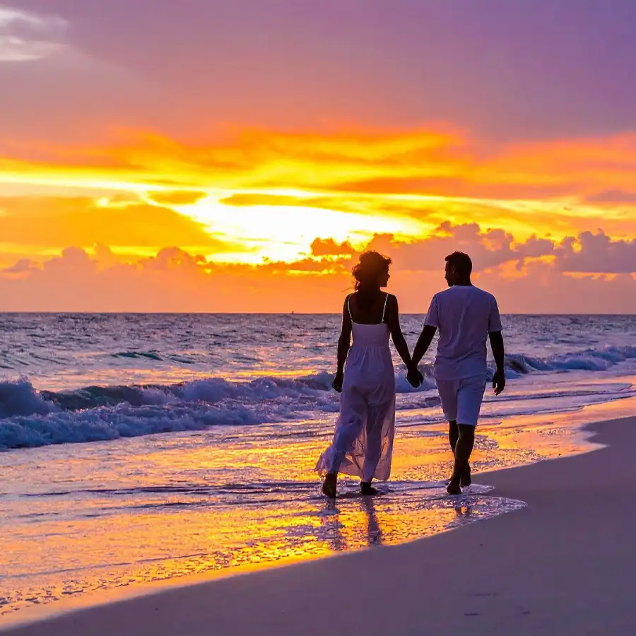 Coppia che cammina sulla spiaggia di Mauritius al tramonto con cielo arancione e mare sullo sfondo