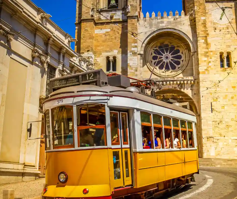 Offerta viaggio Portogallo Classico: viaggio organizzato tra Lisbona e città storiche Tram giallo storico a Lisbona che passa davanti a una chiesa nel centro città