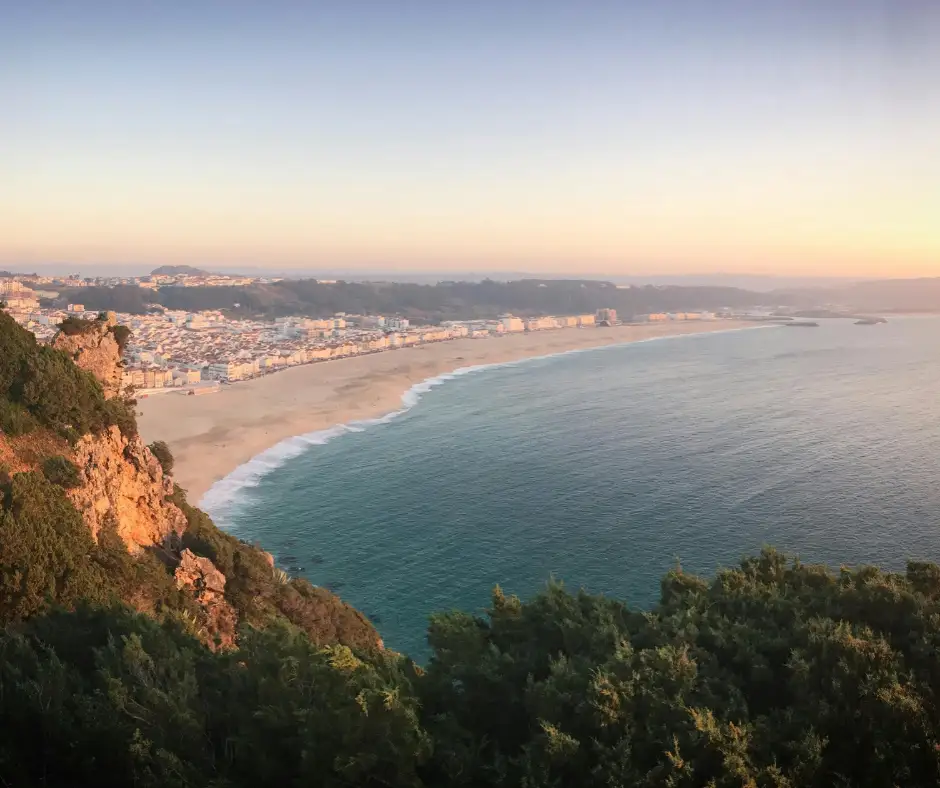 Offerta viaggio Portogallo Classico: pacchetto vacanza tra Nazaré e costa atlantica Panorama della costa di Nazaré con spiaggia, oceano e case lungo la baia al tramonto