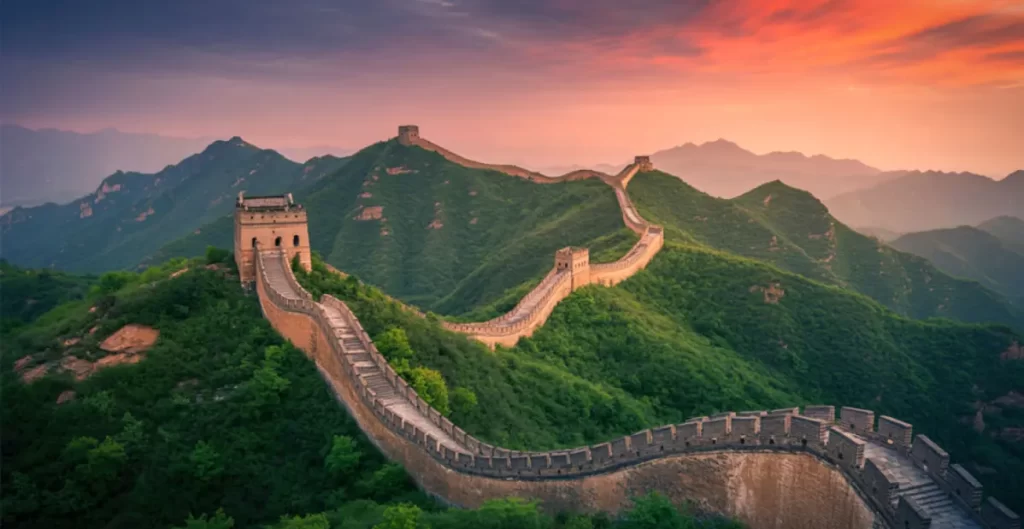 Grande Muraglia della Cina al tramonto tra montagne verdi e cielo cinematografico