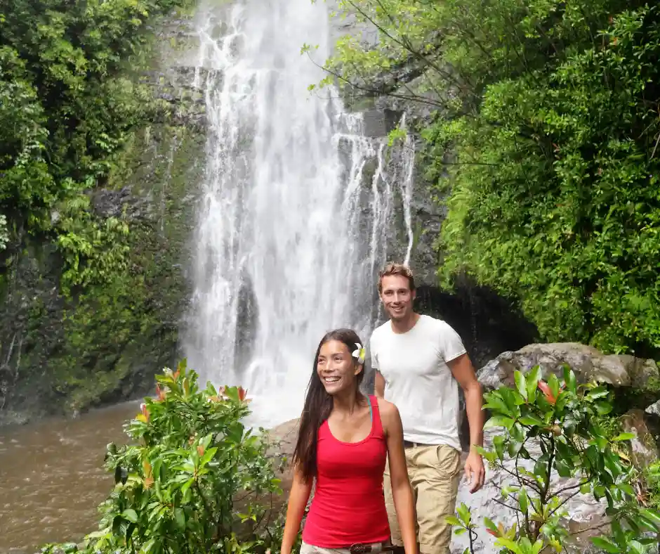 Offerta viaggio Hawaii – Cascate della Road to Hana Viaggiatori davanti a una cascata tropicale lungo la Road to Hana a Maui.