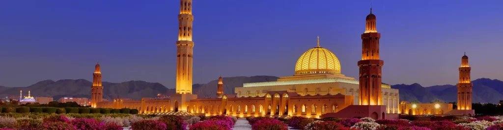 Grande Moschea del Sultano Qaboos illuminata al tramonto a Muscat, in Oman.