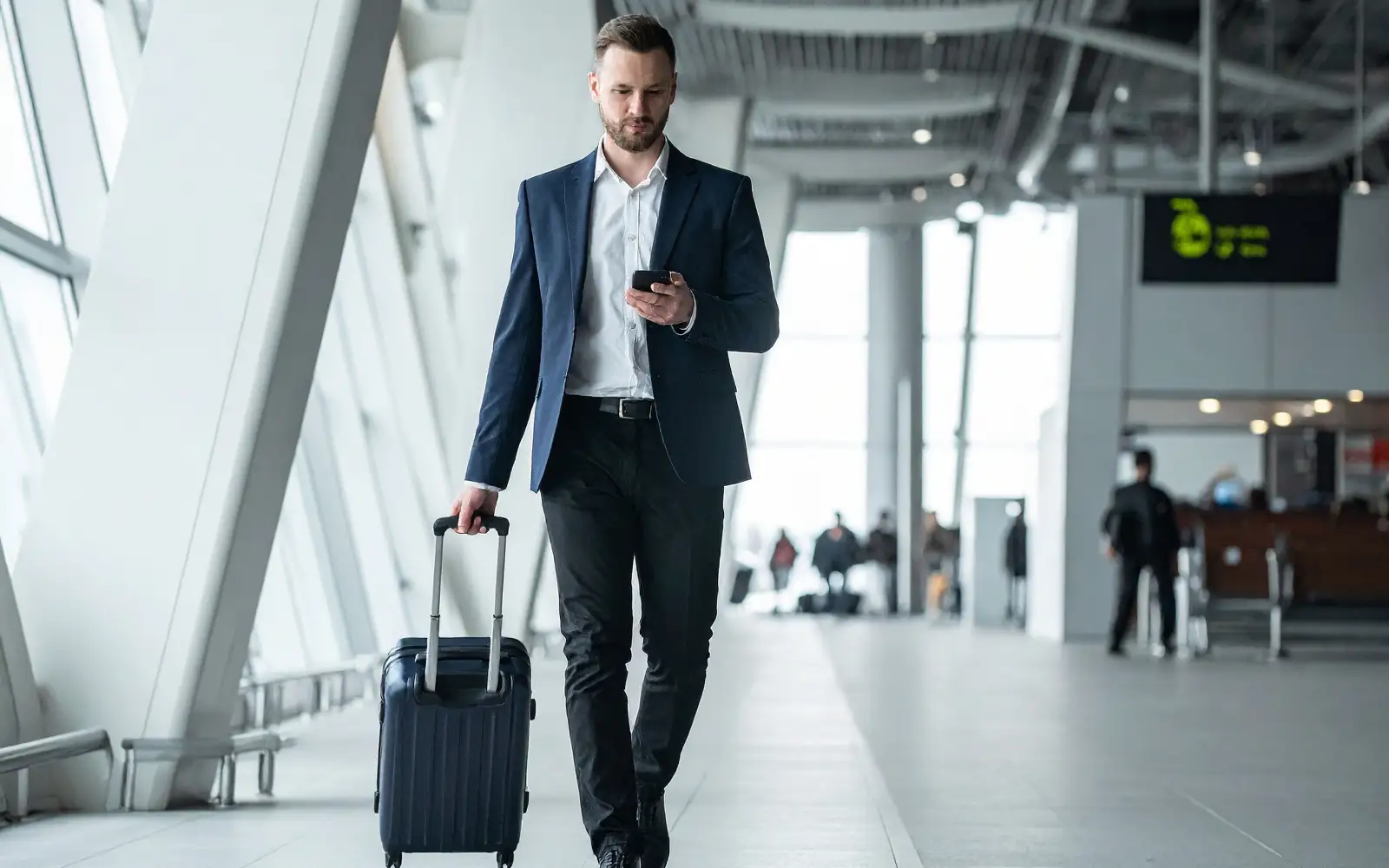 Viaggiatore con trolley consulta lo smartphone mentre attraversa un terminal aeroportuale