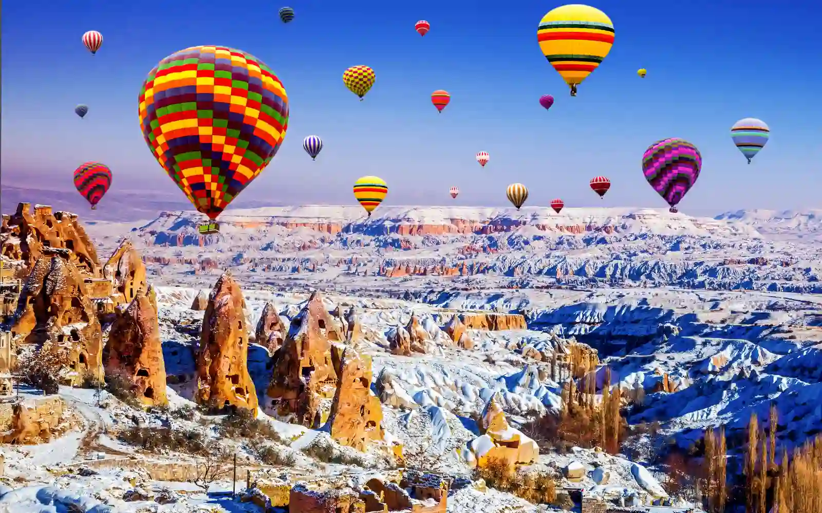 Mongolfiere colorate sorvolano il paesaggio innevato e le formazioni rocciose della Cappadocia