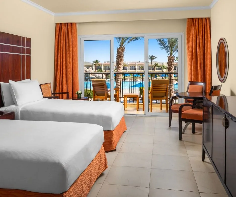 Camera con vista piscina – DoubleTree Sharm Camera con due letti, balcone arredato e affaccio sulla piscina del resort.