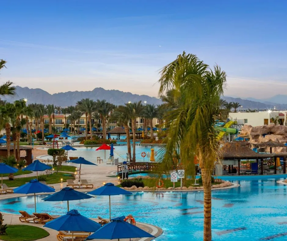 Piscine del DoubleTree by Hilton Sharm Ampia area piscine con palme, lettini e montagne sullo sfondo a Sharm el-Sheikh.
