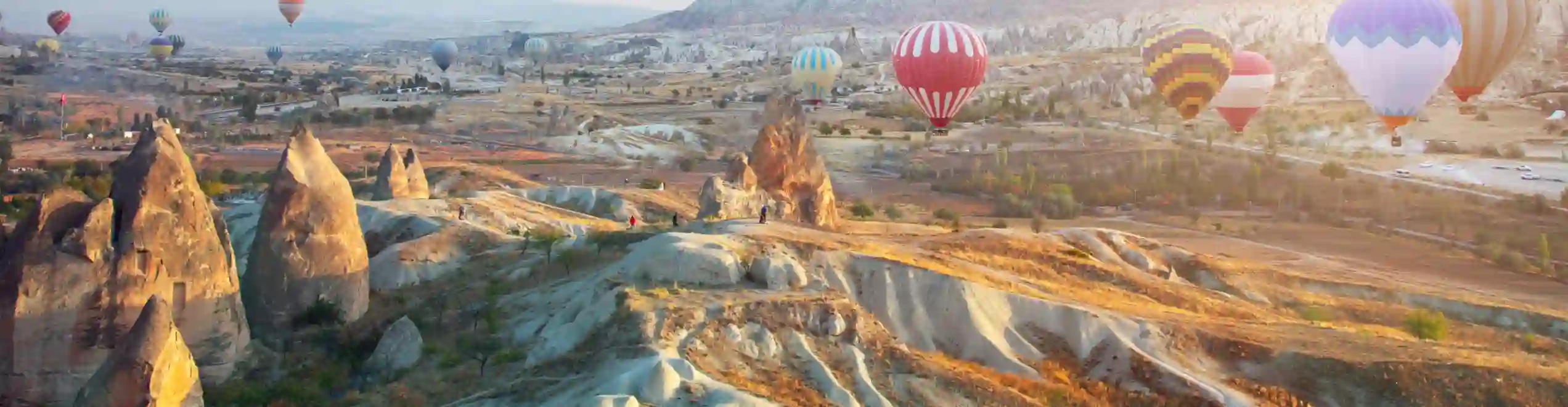 Mongolfiere colorate sorvolano il paesaggio roccioso della Cappadocia nella luce dell'alba.