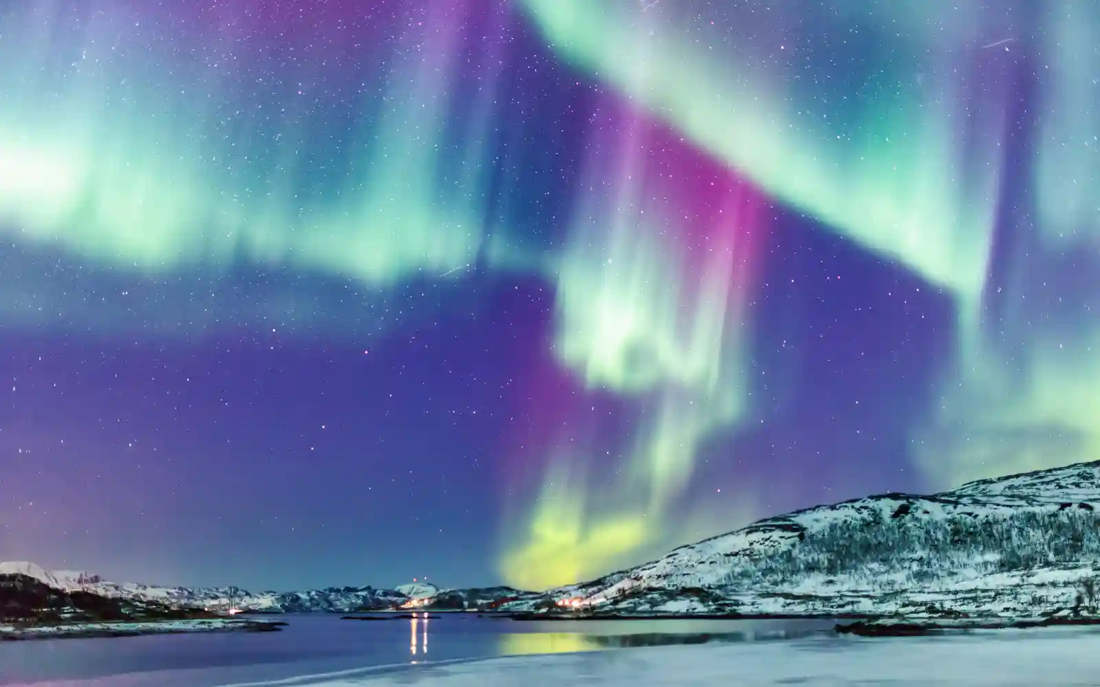 Aurora boreale verde e viola sopra un paesaggio innevato affacciato sull’acqua