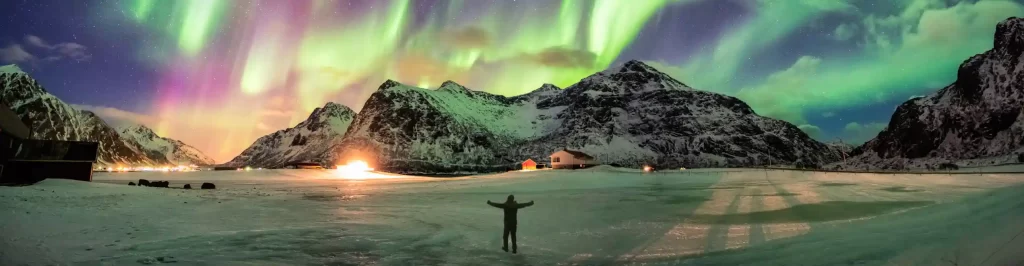 Aurora boreale sopra montagne innevate con una persona nel paesaggio artico.