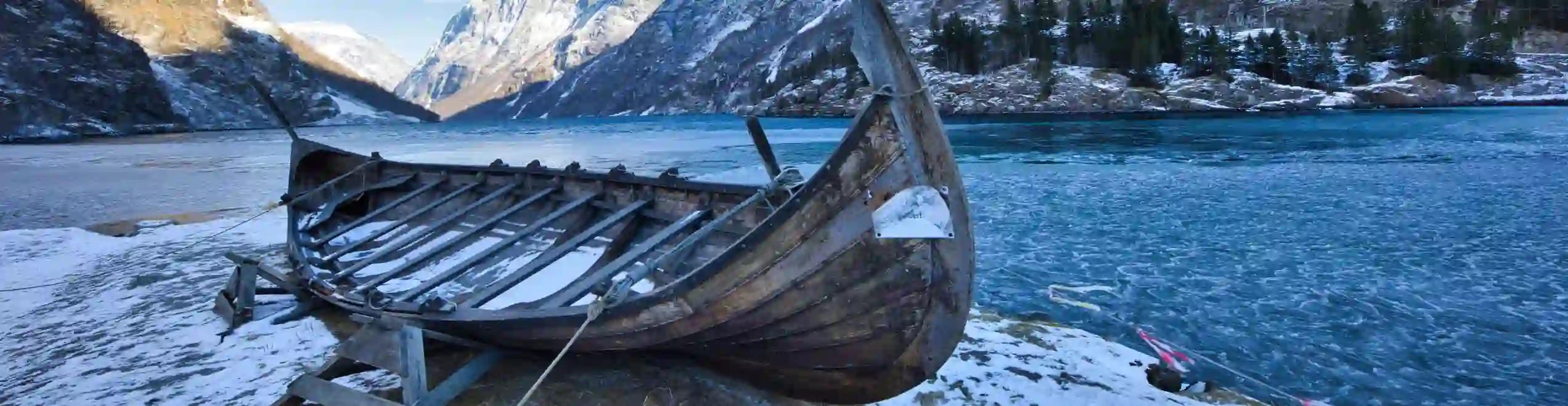 Barca in legno davanti a un fiordo e a ripide montagne innevate.