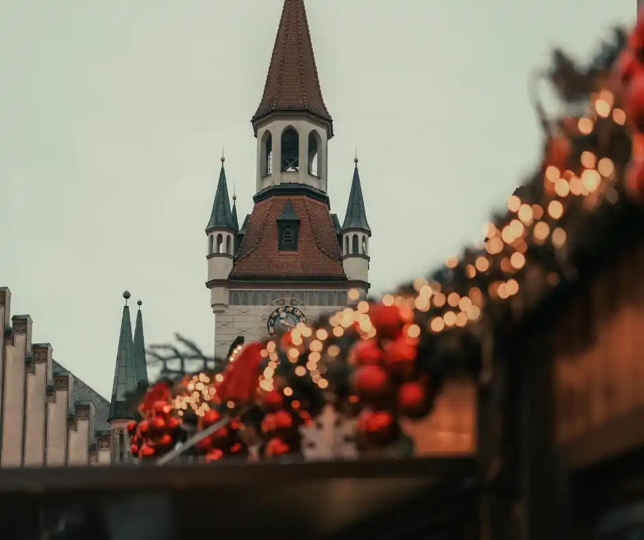 Tra le bancarelle dei mercatini di Natale Bancarelle natalizie illuminate lungo una strada acciottolata con una torre storica sullo sfondo.
