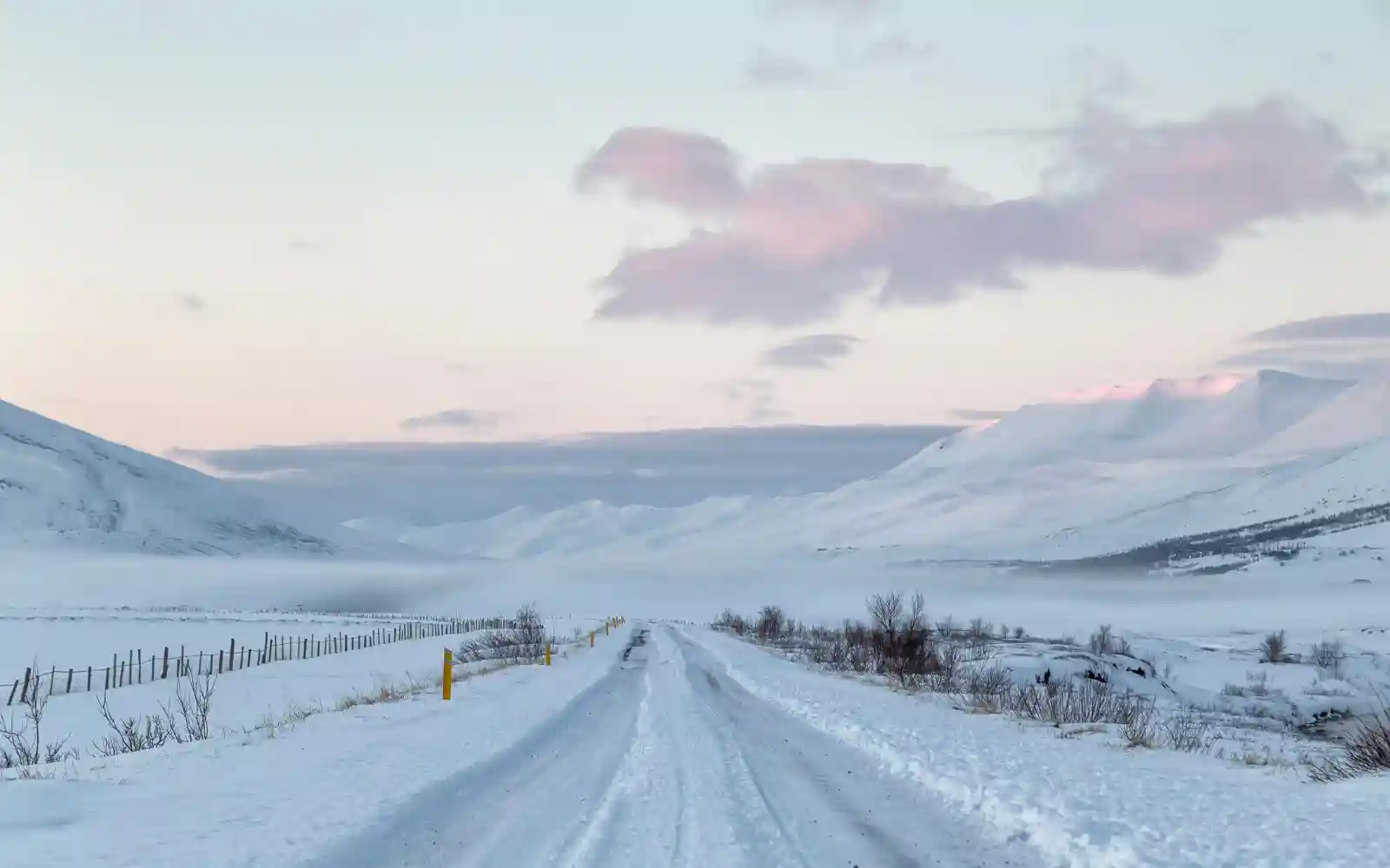 Strada innevata che attraversa una valle circondata da montagne in Islanda