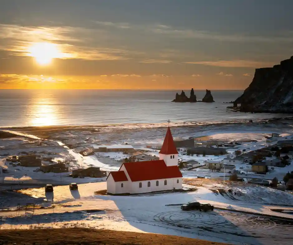 Vík e Reynisdrangar Chiesa di Vík nel paesaggio innevato con i faraglioni di Reynisdrangar sul mare.