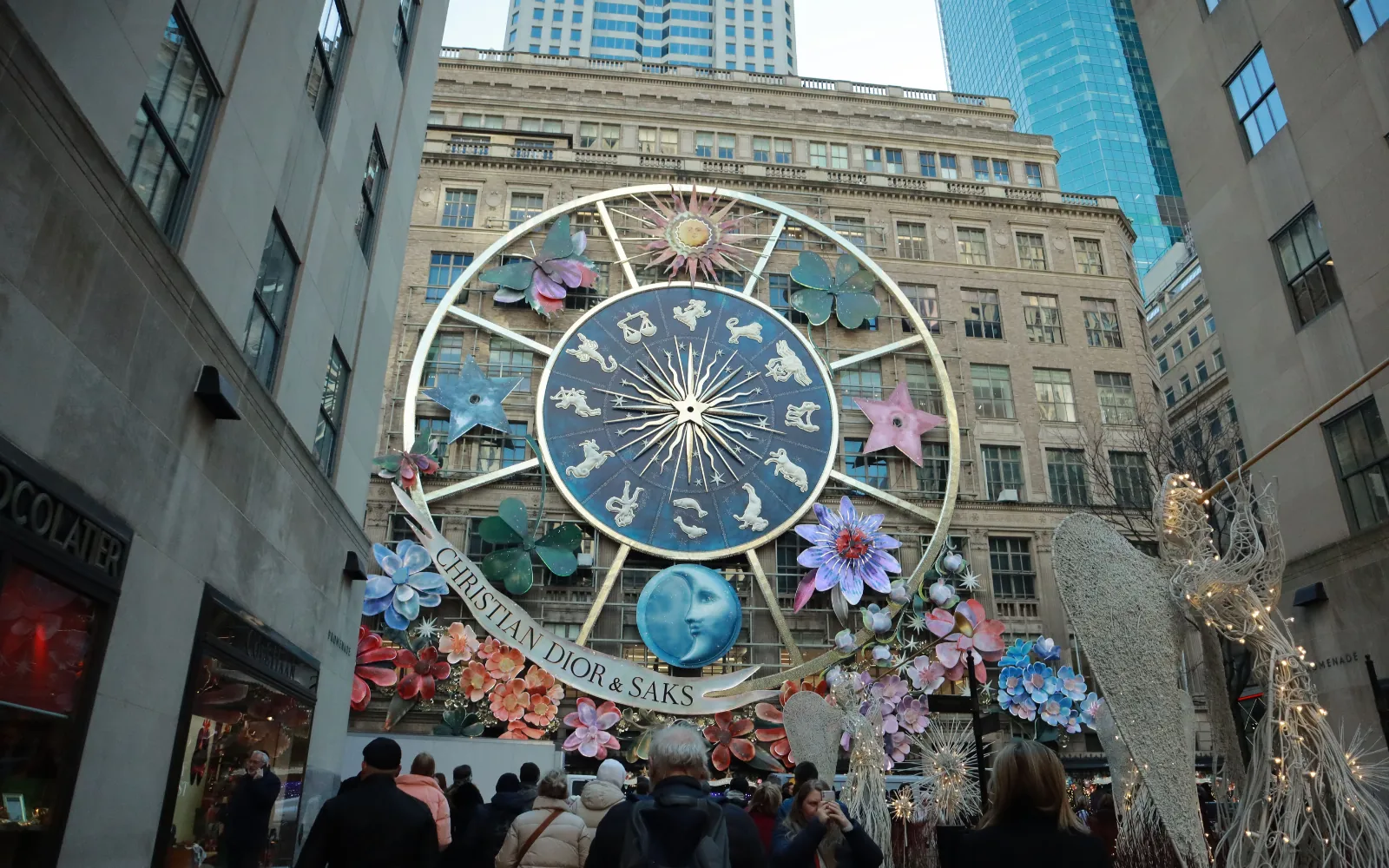 Installazione natalizia con ruota dello zodiaco, fiori e scritta Christian Dior & Saks tra i palazzi di New York