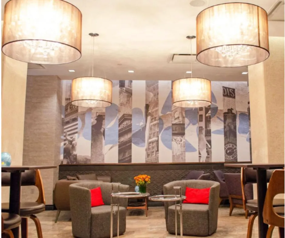 Distrikt Hotel – Lounge Lounge del Distrikt Hotel con poltrone grigie, cuscini rossi e lampade a sospensione.