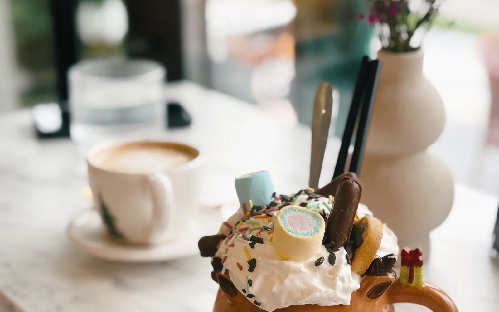Dessert con panna, marshmallow e decorazioni al cioccolato accanto a una tazza di bevanda calda