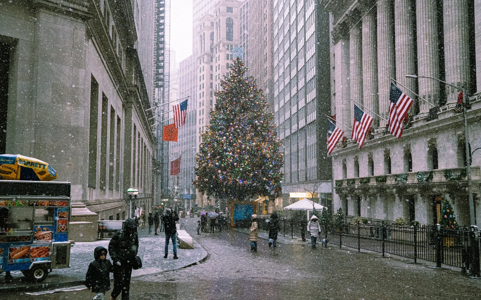 Grande albero di Natale illuminato lungo una strada di New York durante una nevicata, tra passanti e bandiere americane