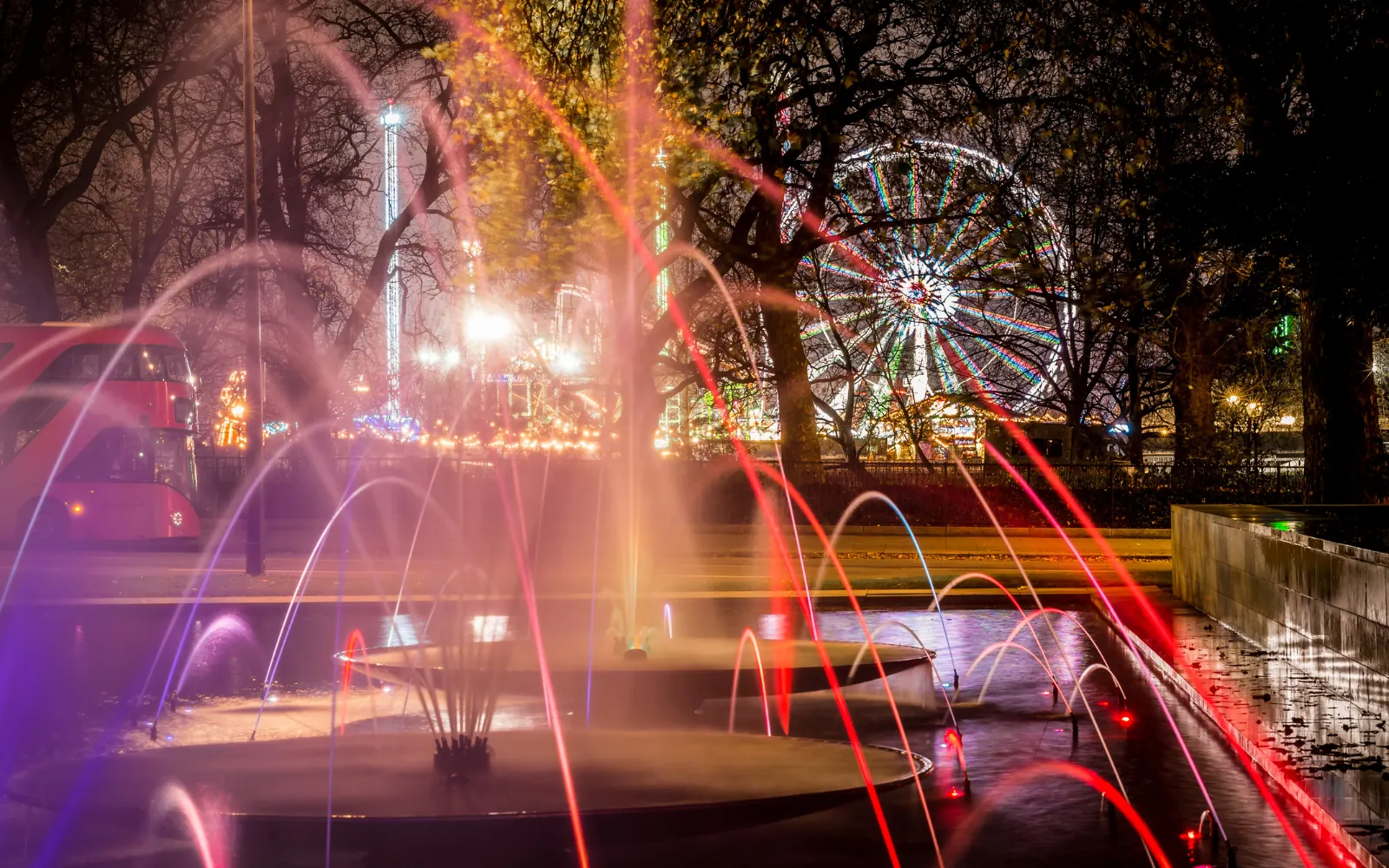 Fontane con getti d'acqua colorati e ruota panoramica illuminata tra gli alberi