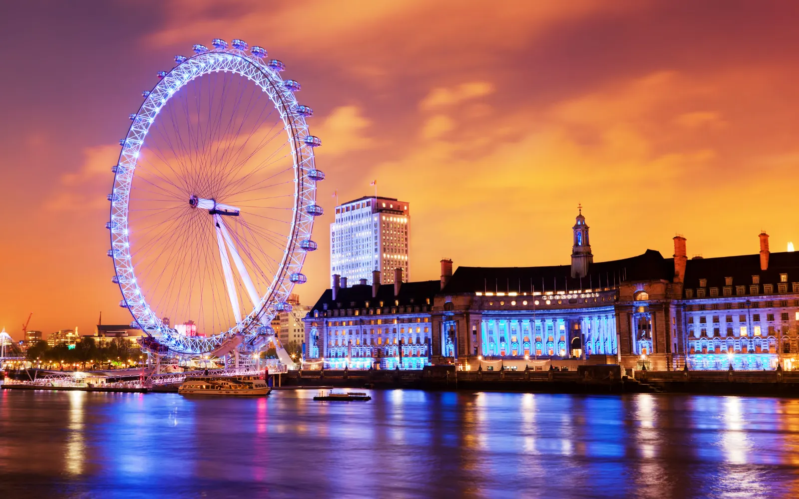 London Eye illuminato sul Tamigi al tramonto, sotto un cielo arancione