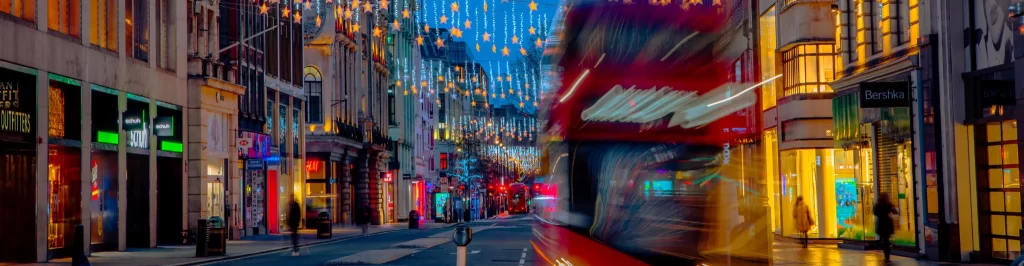 Autobus rosso londinese in movimento lungo una strada commerciale decorata con stelle luminose natalizie.
