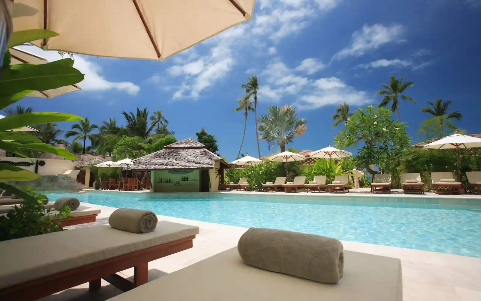 Piscina di un resort di lusso alle Seychelles con lettini, ombrelloni e palme sotto un cielo azzurro
