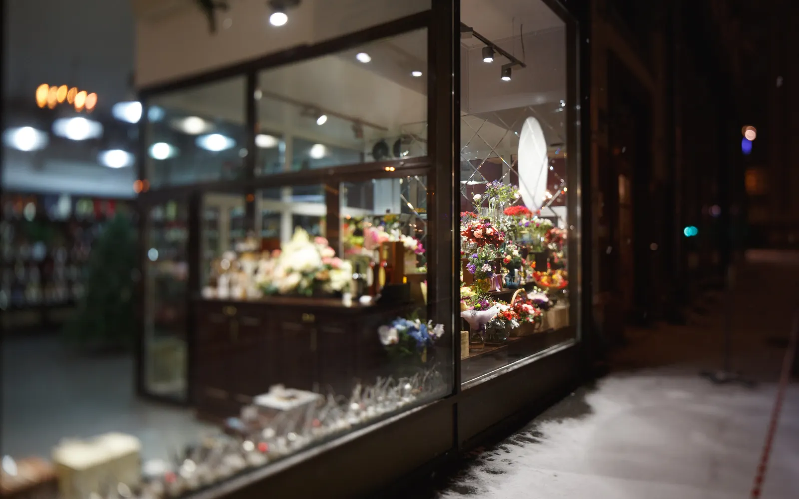 Vetrina di un negozio di fiori illuminata di sera, con neve sul marciapiede